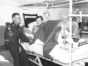 Royal Canadian Army Medical Corps Staff Sergent Medical Assistant chats with patient wounded in Korea